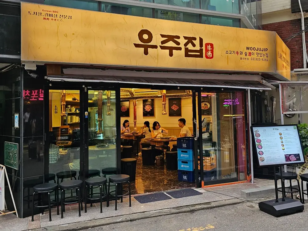 우주집 홍대본점 외부 간판 — 서교동 골목의 노란 간판과 통창